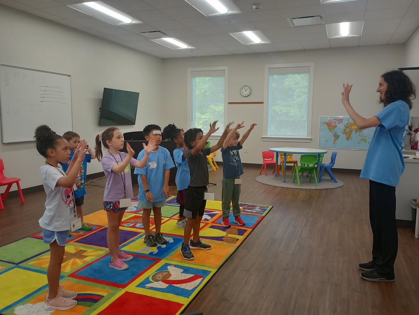 The preschool room in worship, hands raised on the bright rug